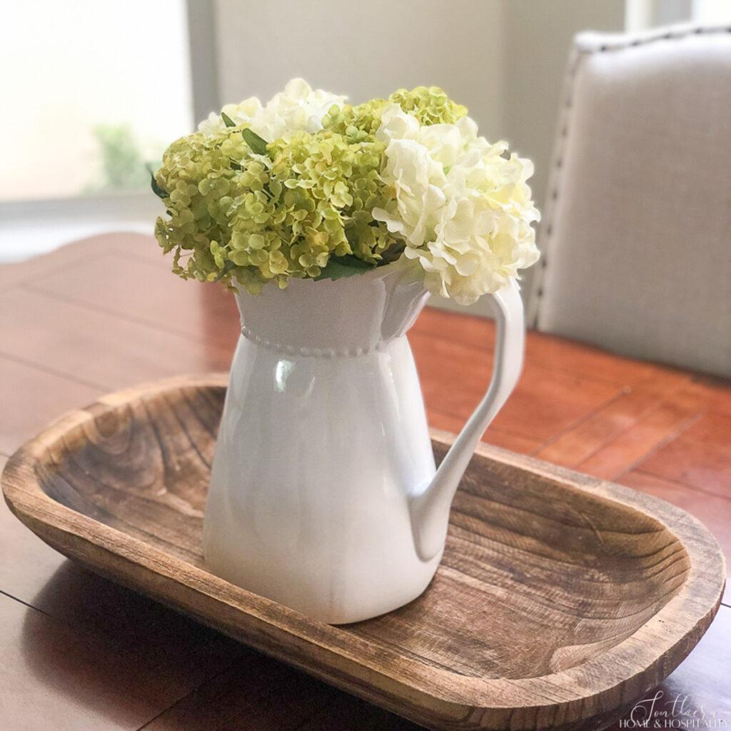 Table centerpiece with green and white hydrangeas in a white pitcher on a dough bowl