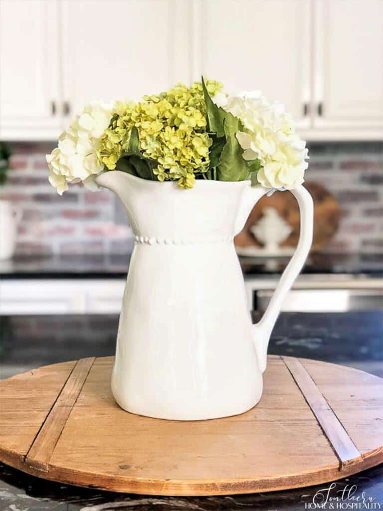 Green and white hydrangeas in white pitcher on kitchen counter