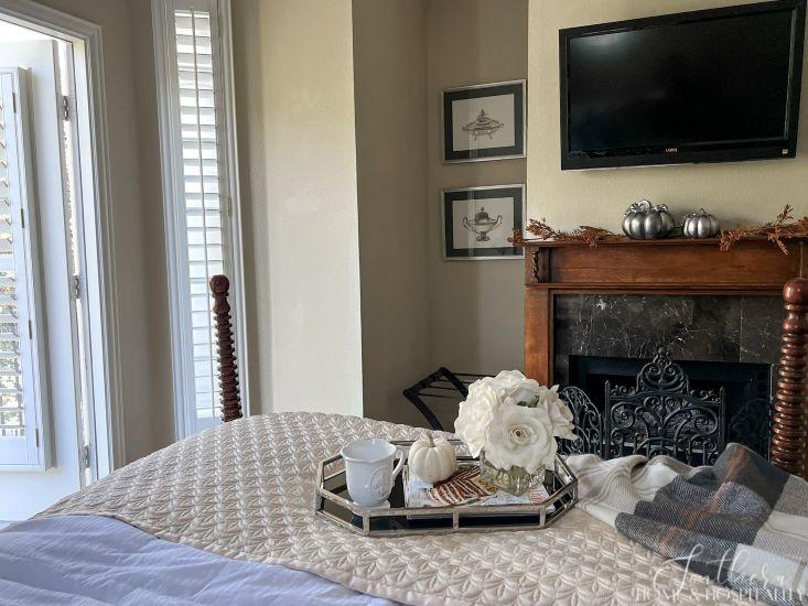 guest bedroom bed with tray of flowers and magazines, fireplace with tv