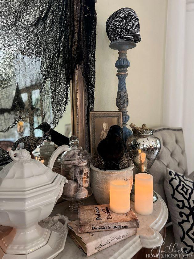 Halloween sideboard decorations with crow, skulls in apothecary jar, books, candles