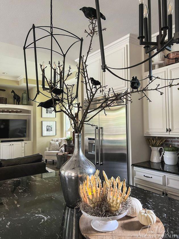 Halloween decorations on kitchen island with crows on branches in vase, skeleton hands around candle