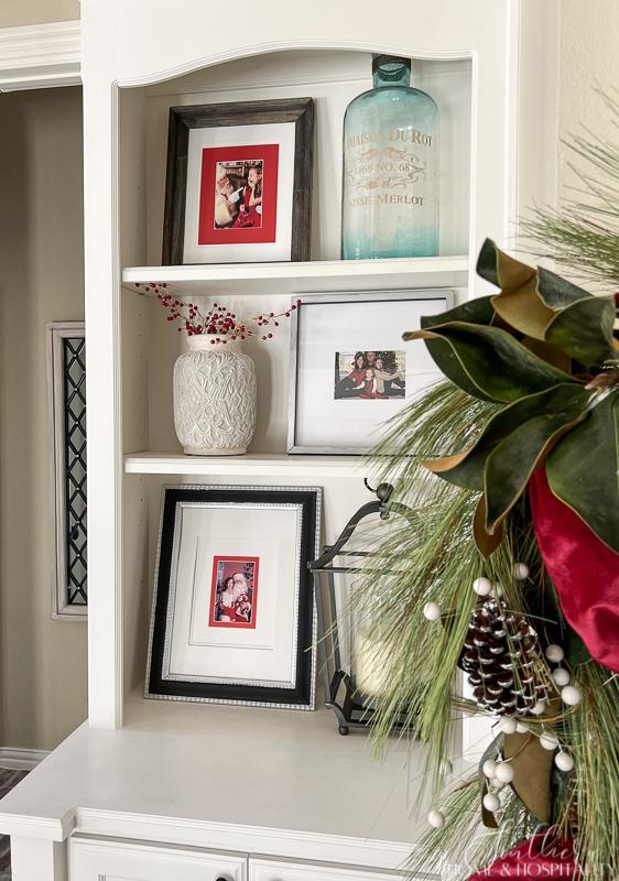 family room shelves with Christmas decorations, family Christmas photos, red berries in white vase, magnolia and pine garland