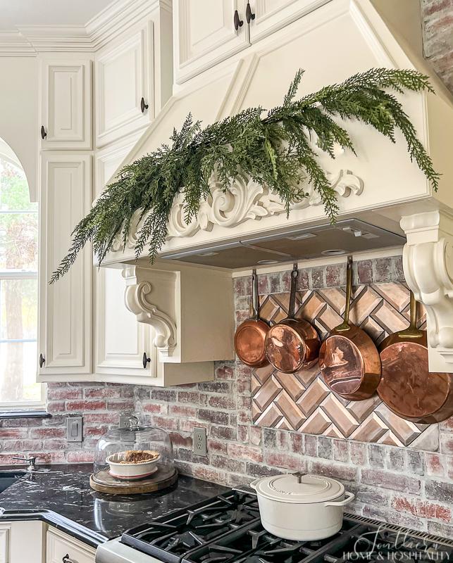French country range hood with Christmas greenery, copper pots and brick backsplash
