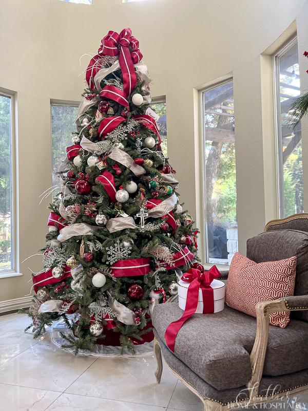 Christmas tree with red and champagne ribbon and red, silver, and white ornaments beside French bergere chair