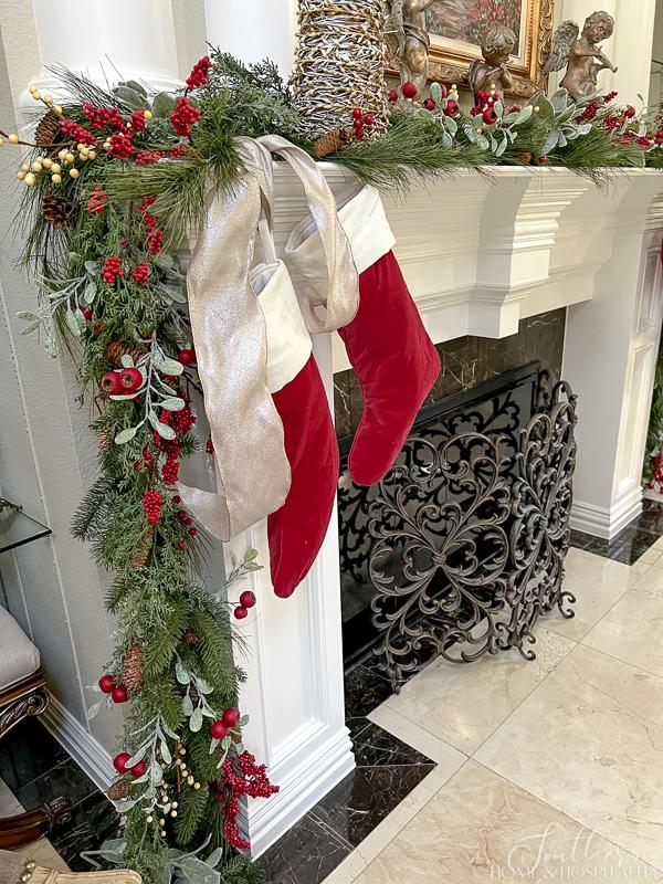 fireplace mantel with Christmas garland of mixed greenery and red and white berries and stockings