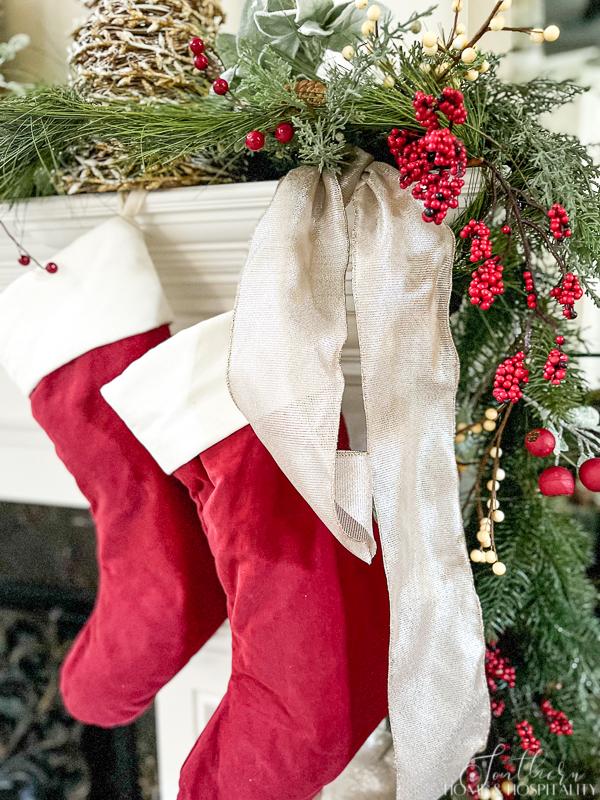 red and white Christmas stockings hung with champagne ribbon next to garland of greenery and red and white berries