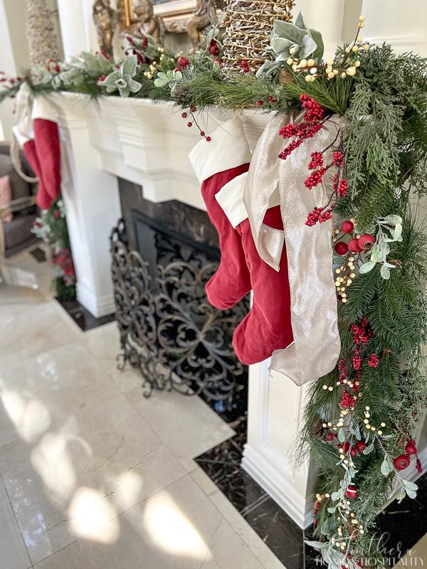 red and white Christmas stockings hung on fireplace mantel with ribbon, mixed greenery with red and white berry garland on mantel