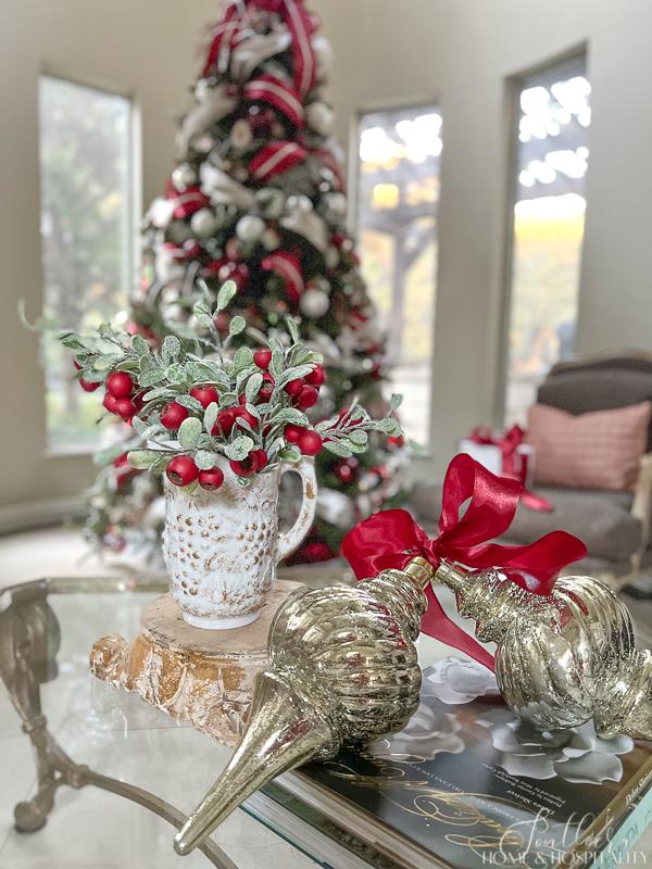oversized mercury glass ornaments tied with ribbon and antique pitcher of frosted greenery and red berries on coffee table