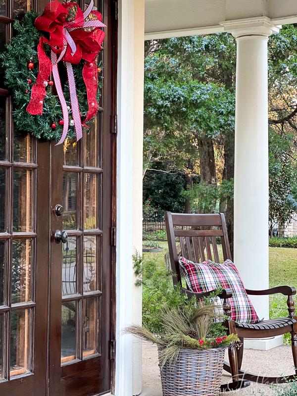 porch rocker with plaid pillow, Christmas wreath and basket of greenery