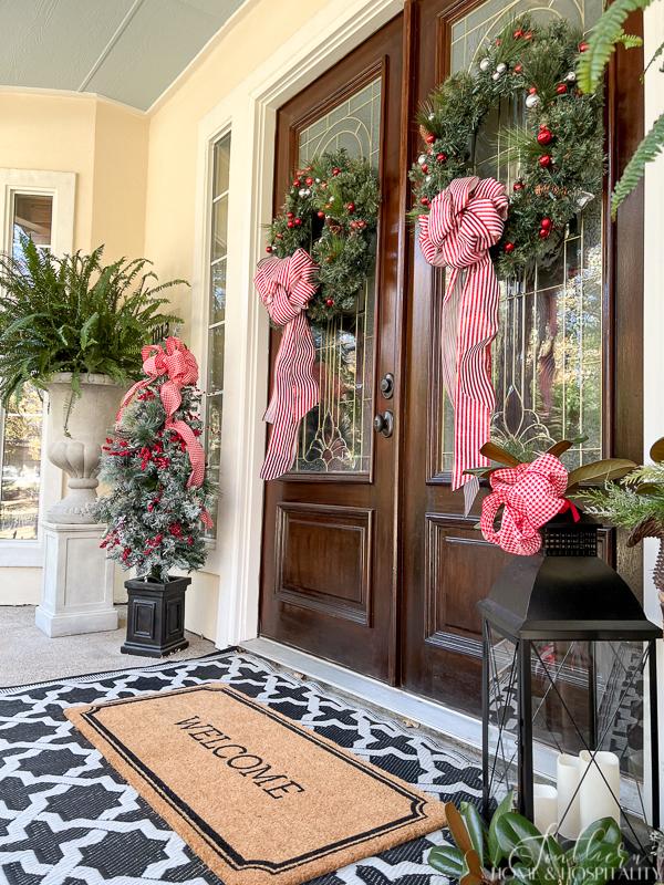 double wreaths on front doors with red and white bows, welcome mat, large lantern