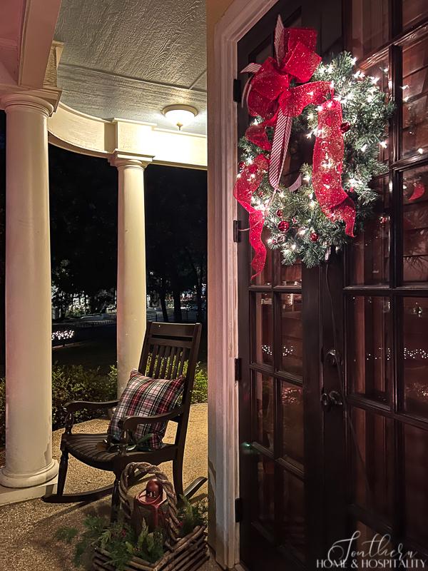 lighted Christmas wreath on french doors, porch rocker with plaid pillow