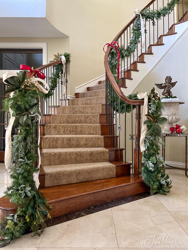 Staircase with Christmas garland of mixed greenery and ribbon sweeping the floor and swooping up the banisters
