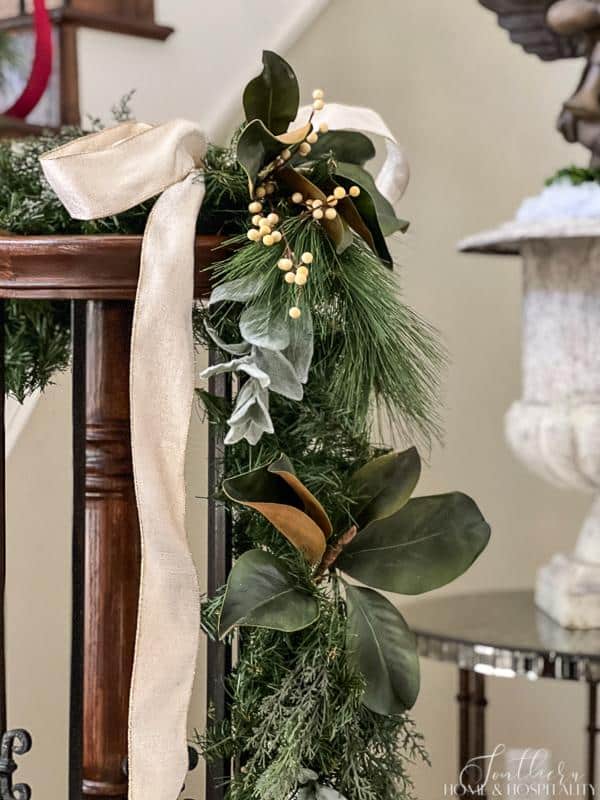 Staircase with closeup of Christmas garland on newel post of mixed greenery, pine, magnolia, cedar, white berries, and ribbon