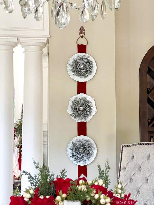 Triple Christmas wreaths on plates hung on red ribbon on the wall