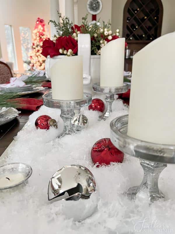 red and white Christmas table red roses in white bowl red wreath snow candles jingle bell