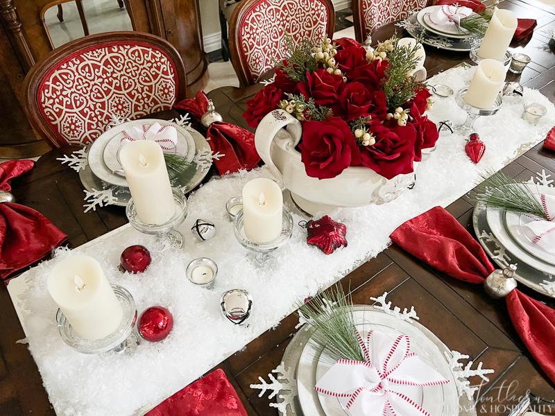 red and white Christmas table red roses in white bowl red wreath snow candles