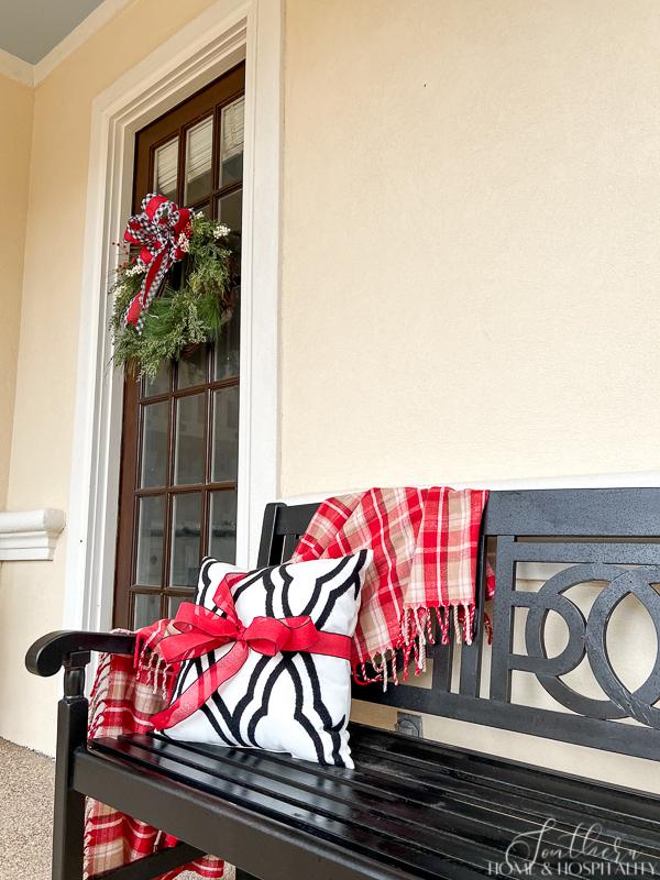 black porch bench with plaid blanket and pillow tied with red bow