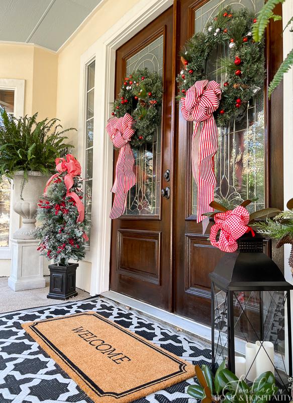 front doors with Christmas wreaths welcome mat lantern Christmas tree