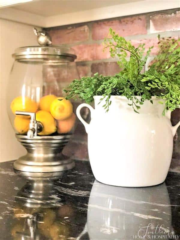 lemons in drink dispenser, fern in white pot on black granite kitchen counter