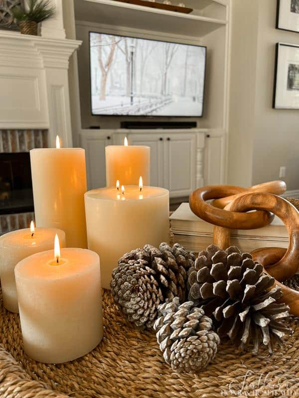 winter coffee table arrangement on wicker tray with candles, pinecones, wood decor, books, winter art on tv