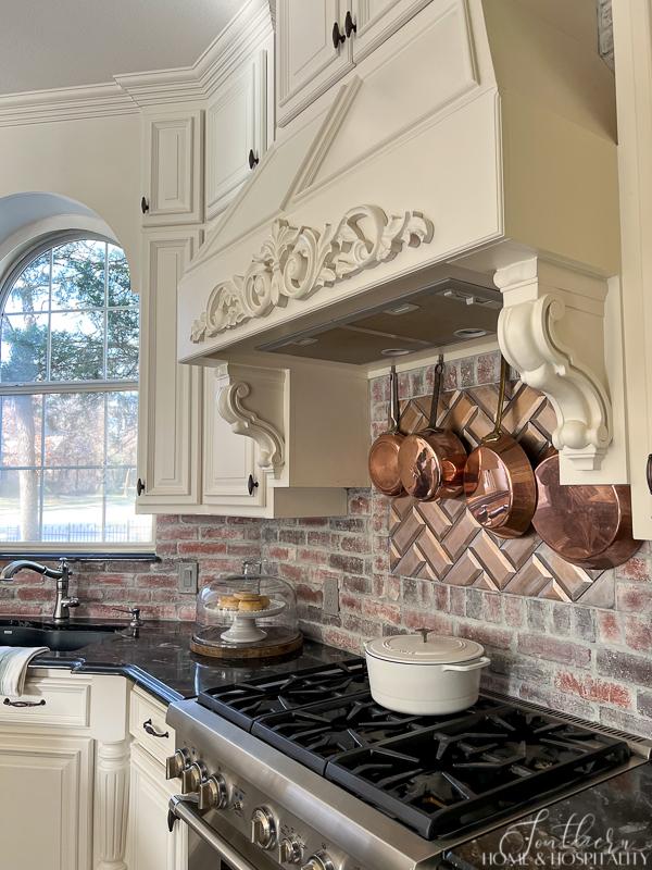 French country kitchen, copper pots under range hood, black granite countertops, brick backsplash