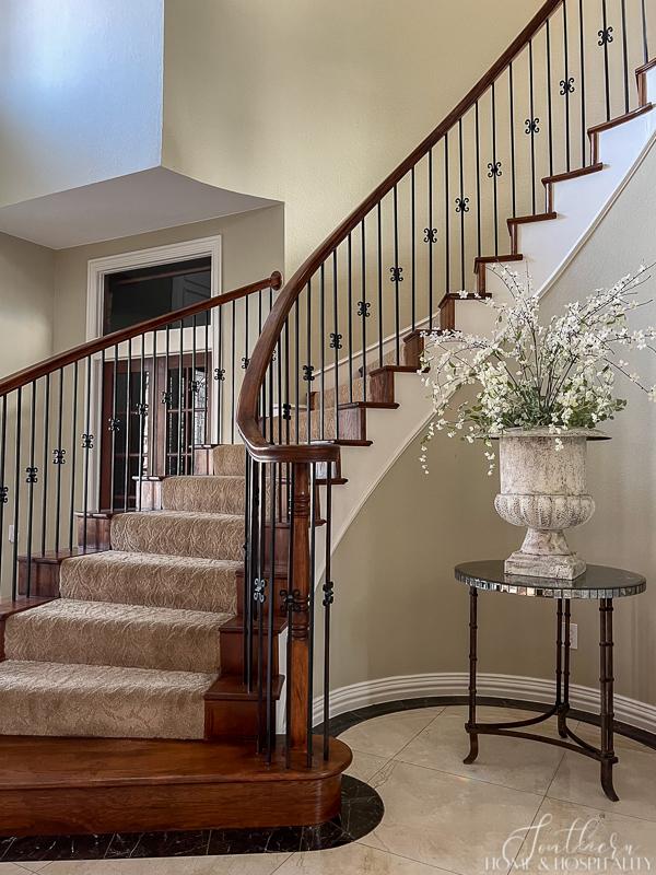 traditional curved staircase with carpet, mirrored round foyer table, French urn with flowers entry decor