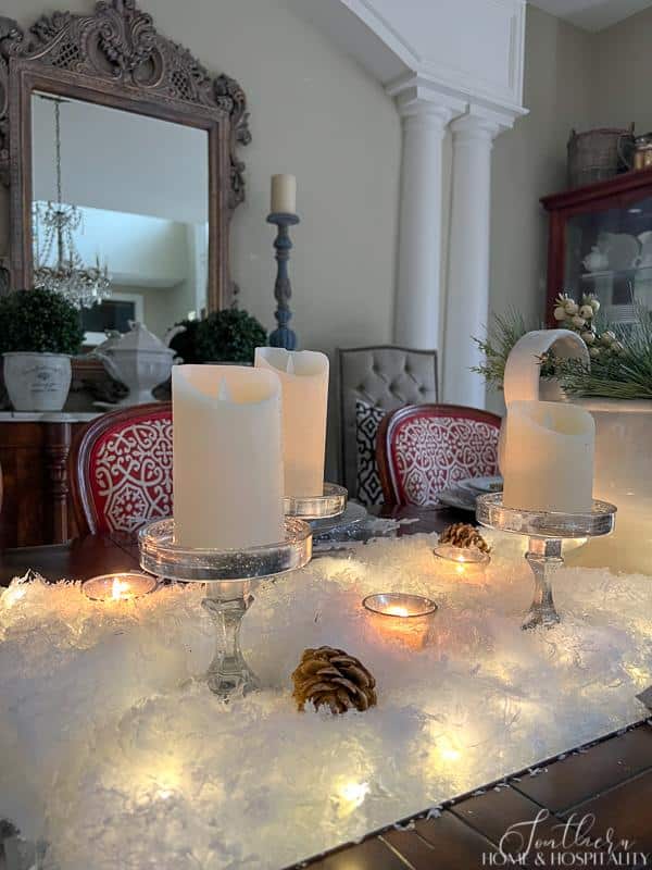 Winter tablescape with snow, candles in mercury glass holders, and winter greenery, French sideboard, ironstone, vintage crystal chandelier