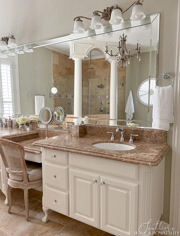 classic master bathroom with furniture vanity and marble counters, travertine