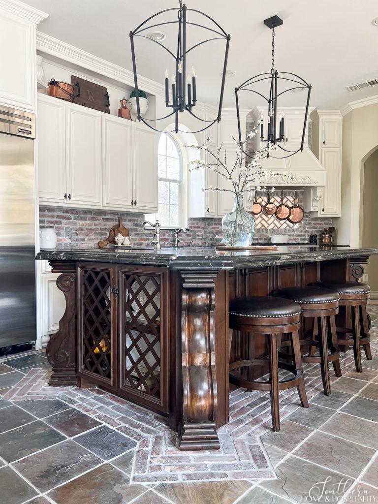 Modern French country kitchen with furniture island, brick backspash, and oversize black iron pendants