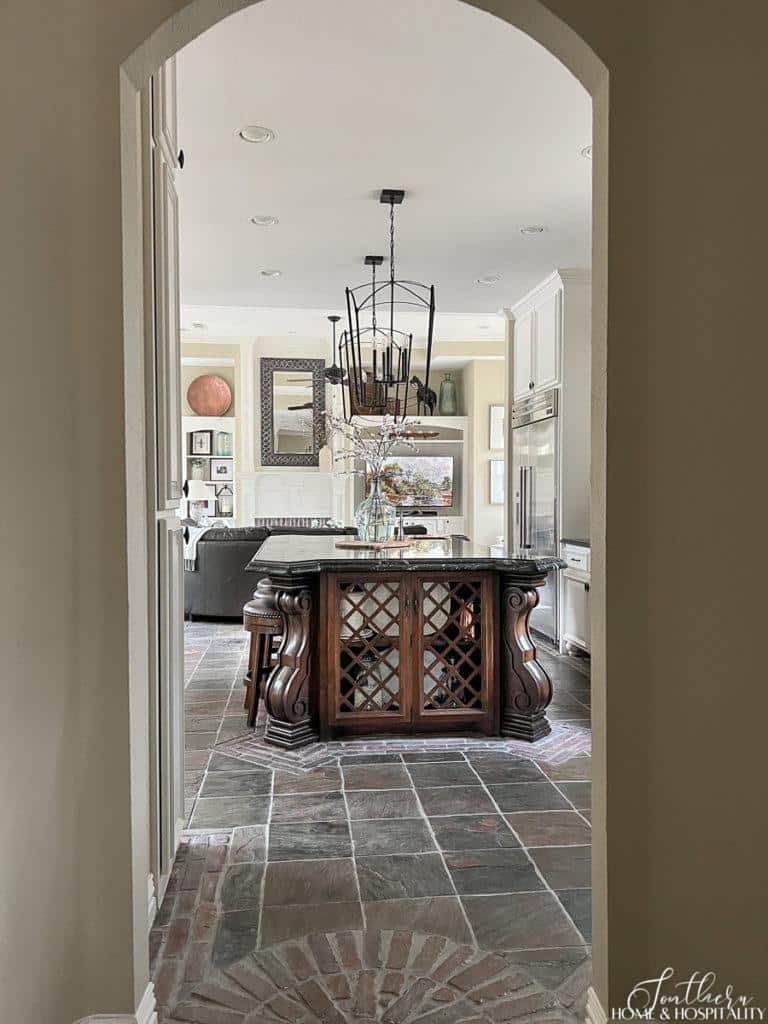 entry to open concept French country kitchen and family room with furniture island and brick and slate floor