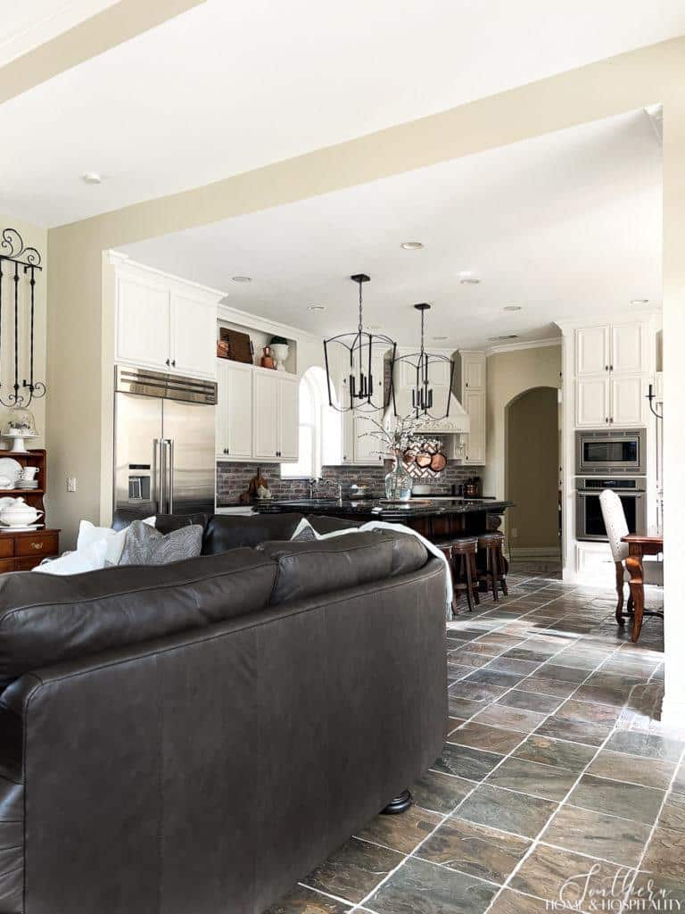 Open concept traditional French country family room and kitchen with slate floor and brick backsplash