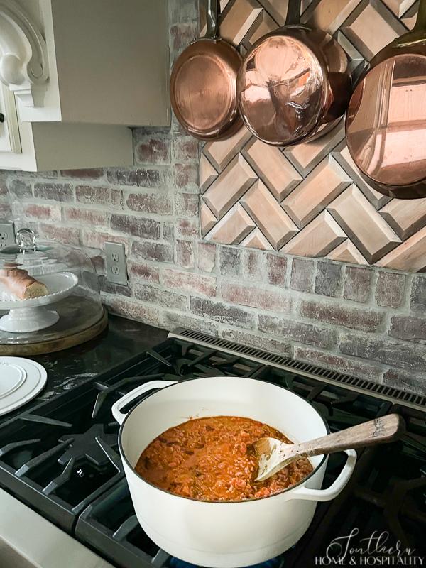 Taco soup cooking on stovetop beside brick backsplash and copper pans