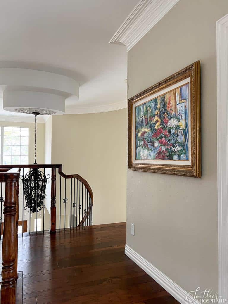 Colorful painting of a flower market in a classic gold frame hung in a hallway in front of stairs
