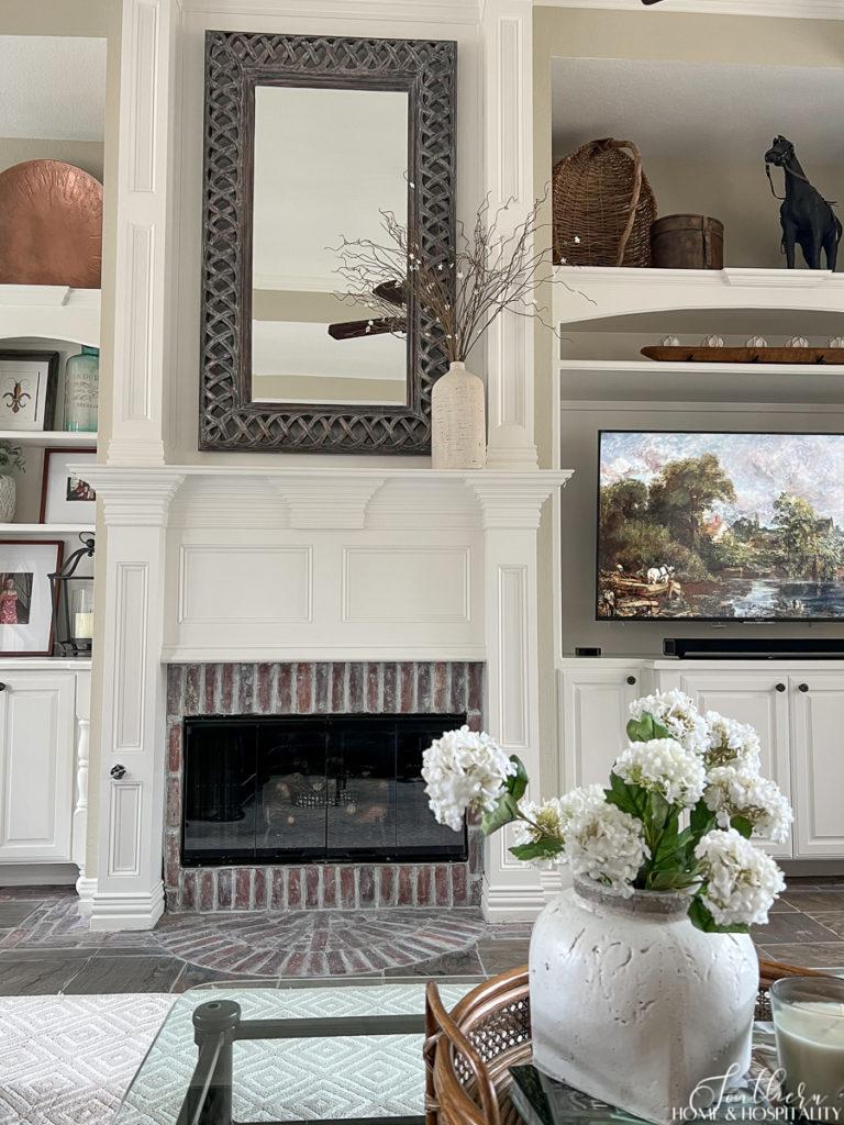 A large mirror hung over a brick and white wood fireplace in a traditional family room