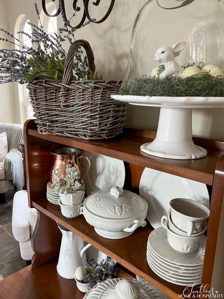 French country hutch with ironstone and an Easter bunny under a cloche beside a basket of lavender