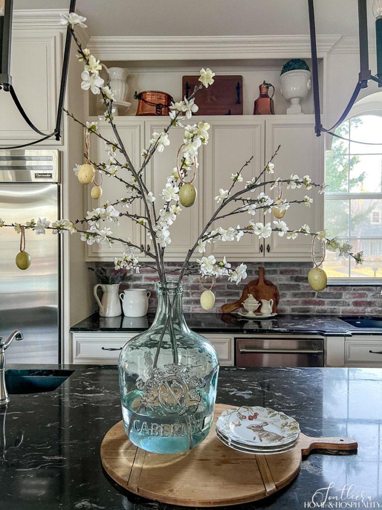 French country kitchen with a glass wine jug filled with flowering branches and easter eggs