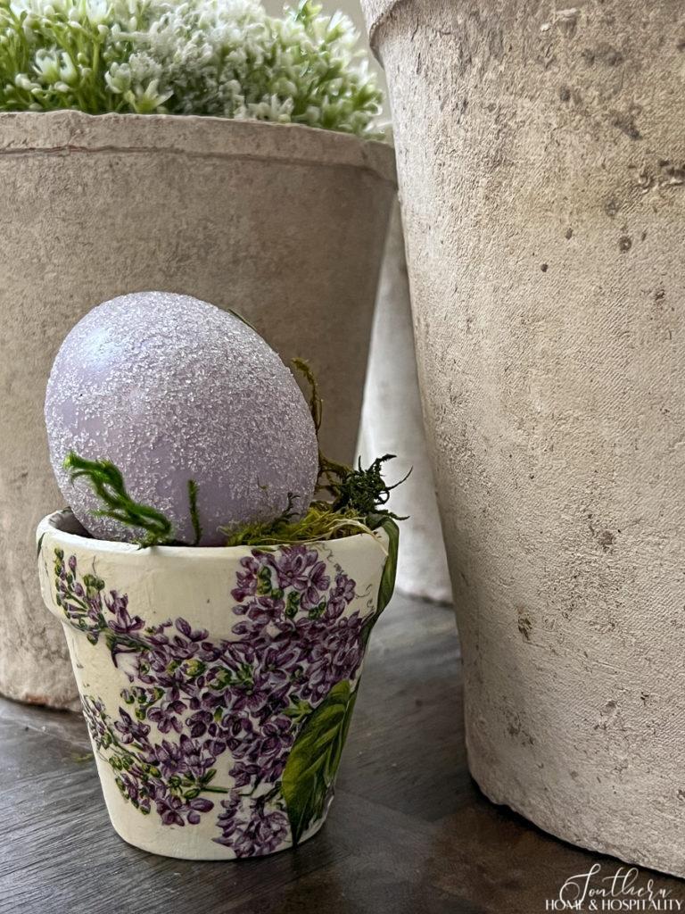 Decoupage flower pot with purple and white flowers holding a purple Easter egg