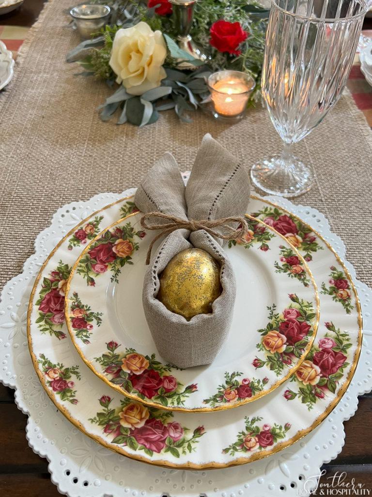 Floral china and bunny napkin fold with gold egg on spring place setting