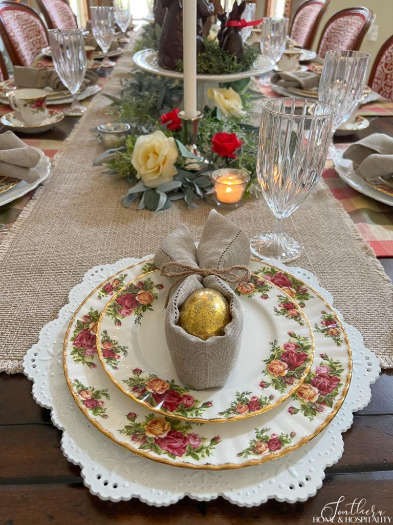 Napkin folded into Easter bunny shape around a gold egg on Old Country Roses china