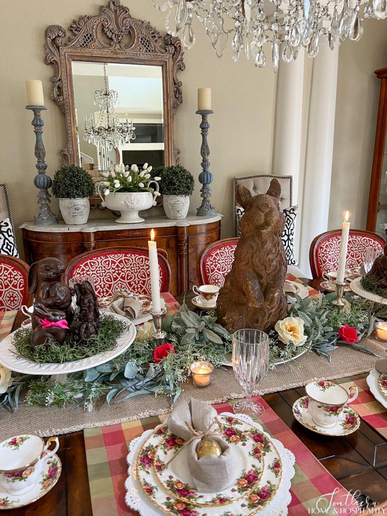 French country dining room decorated for Easter with table set with pink and yellow flowers, china, chocolate bunnies, and bunny napkin fold