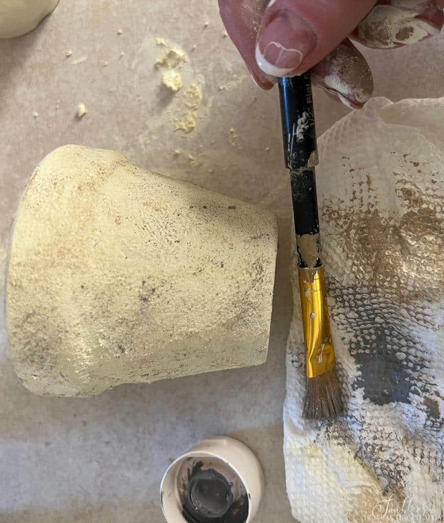 Wiping paint off of brush preparing to dry brush aged spots onto flower pot