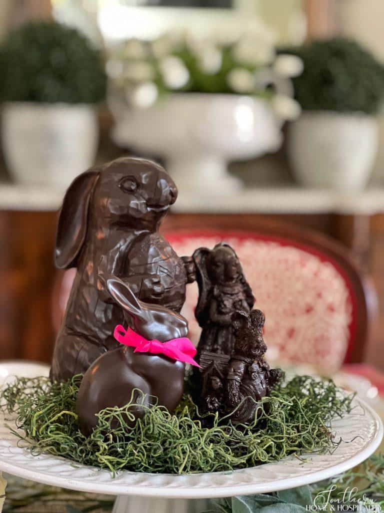 Faux chocolate Easter bunnies on a white cake pedestal with green moss