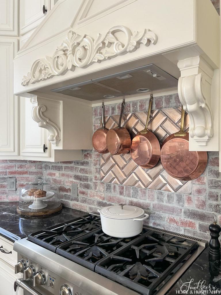 A collection of copper pots hanging over the cooktop in a French country kitchen