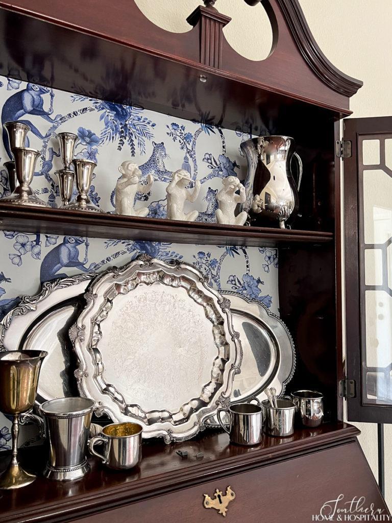 Wood secretary with blue and white chinoiserie wallpaper back filled with vintage silver