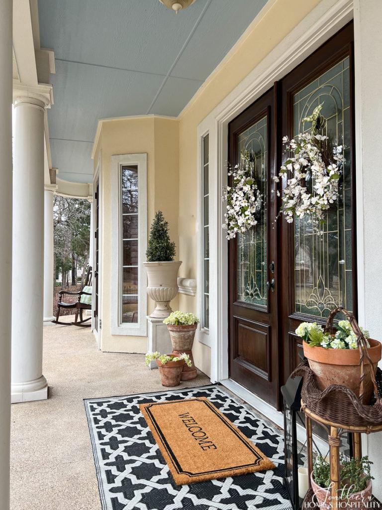 Southern front porch with a haint blue ceiling decorated for spring with white floral door wreaths, spring flowers in garden pots