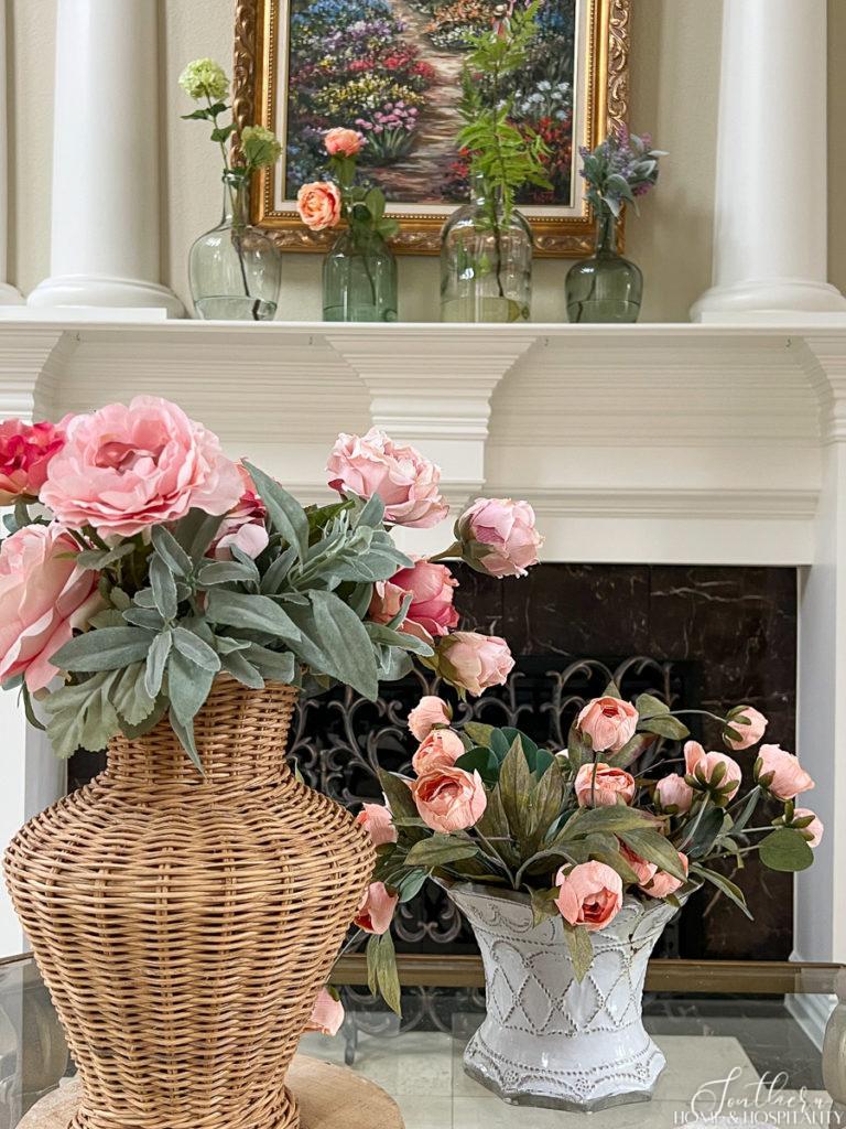 Pink and peach cottage roses in wicker and French pottery in a coffee table vignette and colorful spring flower stems in green and clear glass vases on the mantel