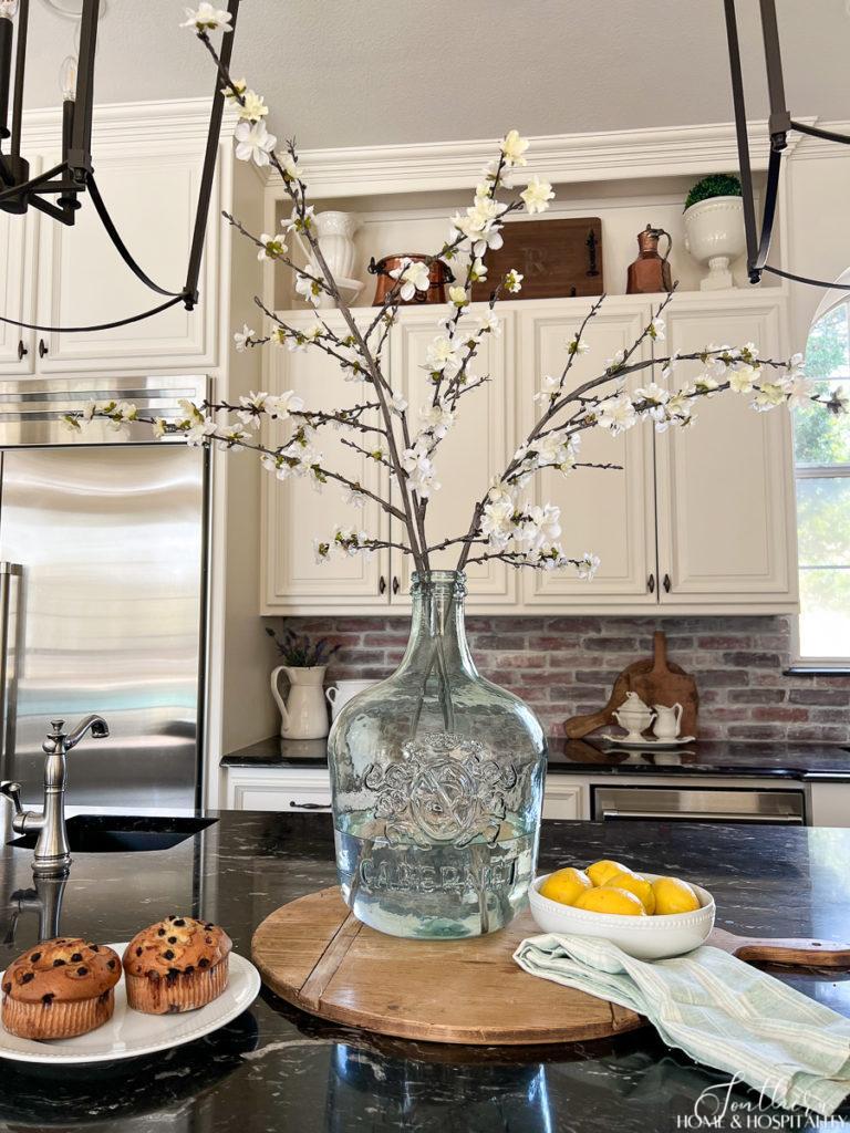 White flowering spring branches in a green glass wine jug in a French country kitchen 