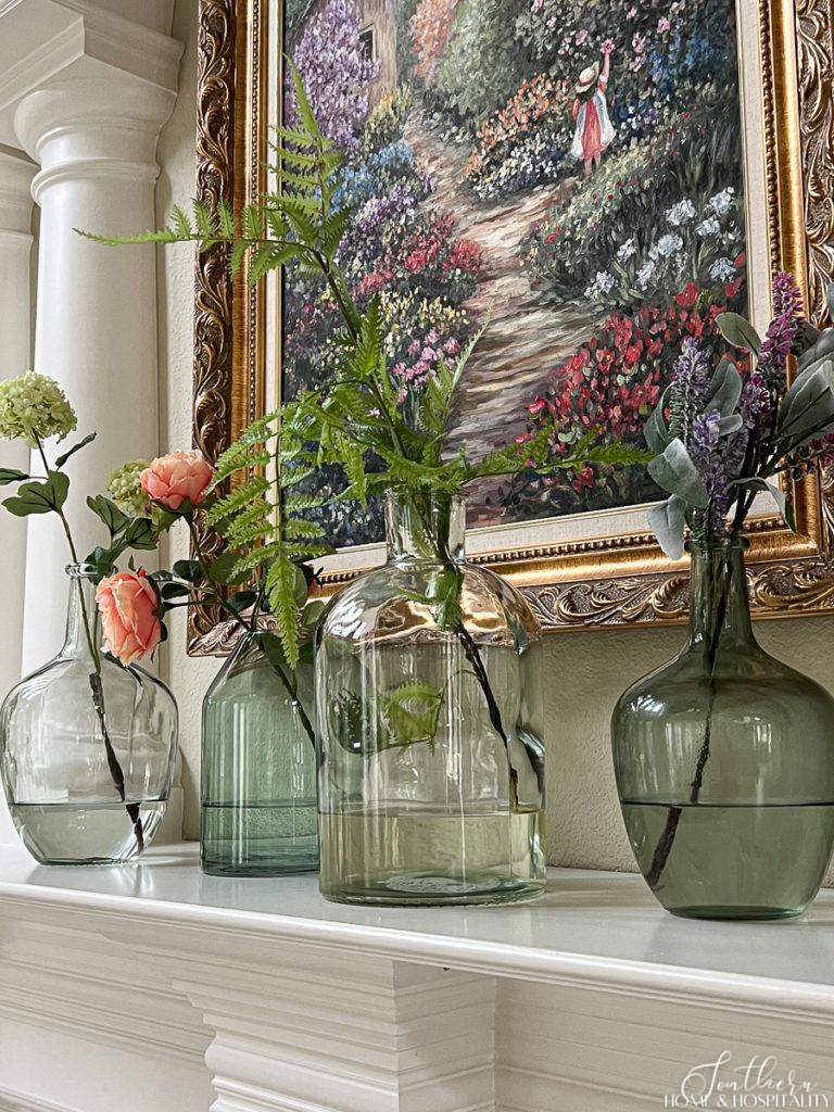 Faux spring floral stems in green and clear glass vases on the living room mantel