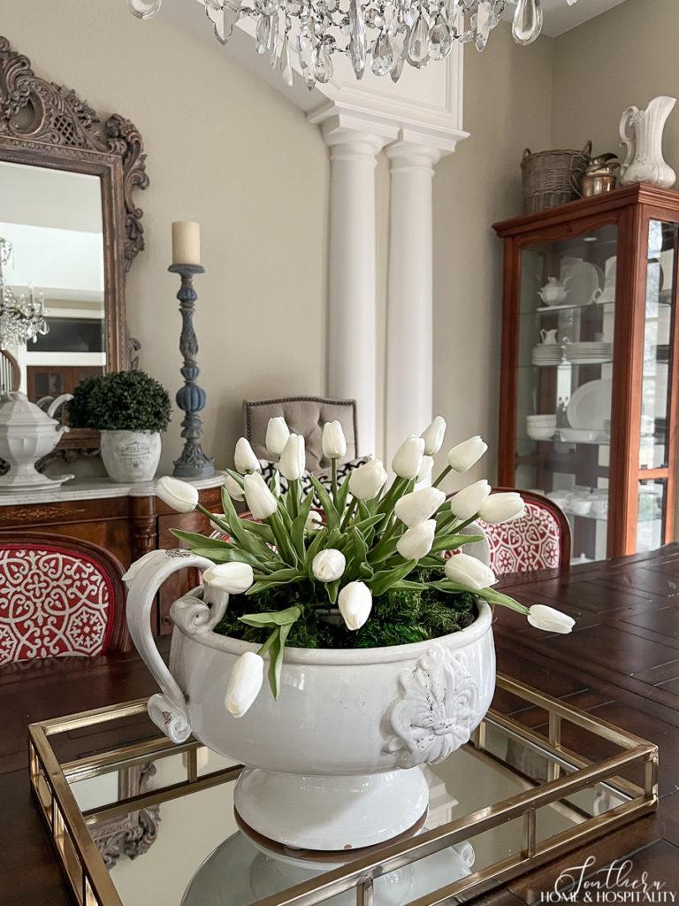 Spring centerpiece with white tulips and moss in a white pedestal bowl in a French inspired dining room
