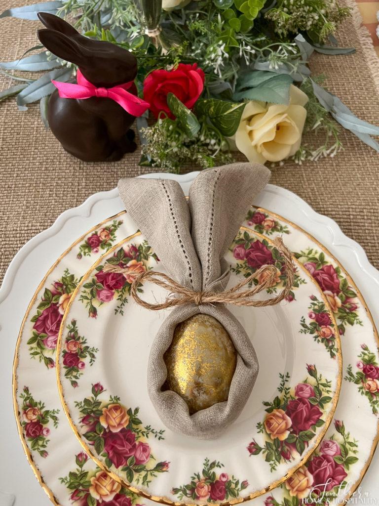 Natural linen napkin tied with twine into bunny ears around a gold egg